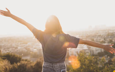 Woman looking toward the sunset with outstretched arms